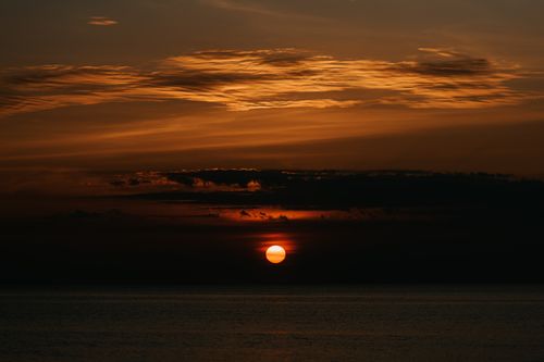 Free A stunning sunset with a dramatic sky reflecting over a serene sea horizon. Stock Photo