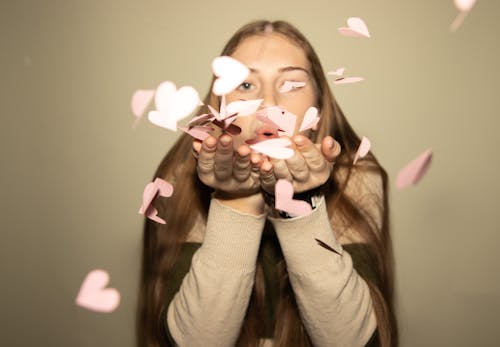 Woman Blowing into Heart Shaped Paper Cutouts in Her Hands 