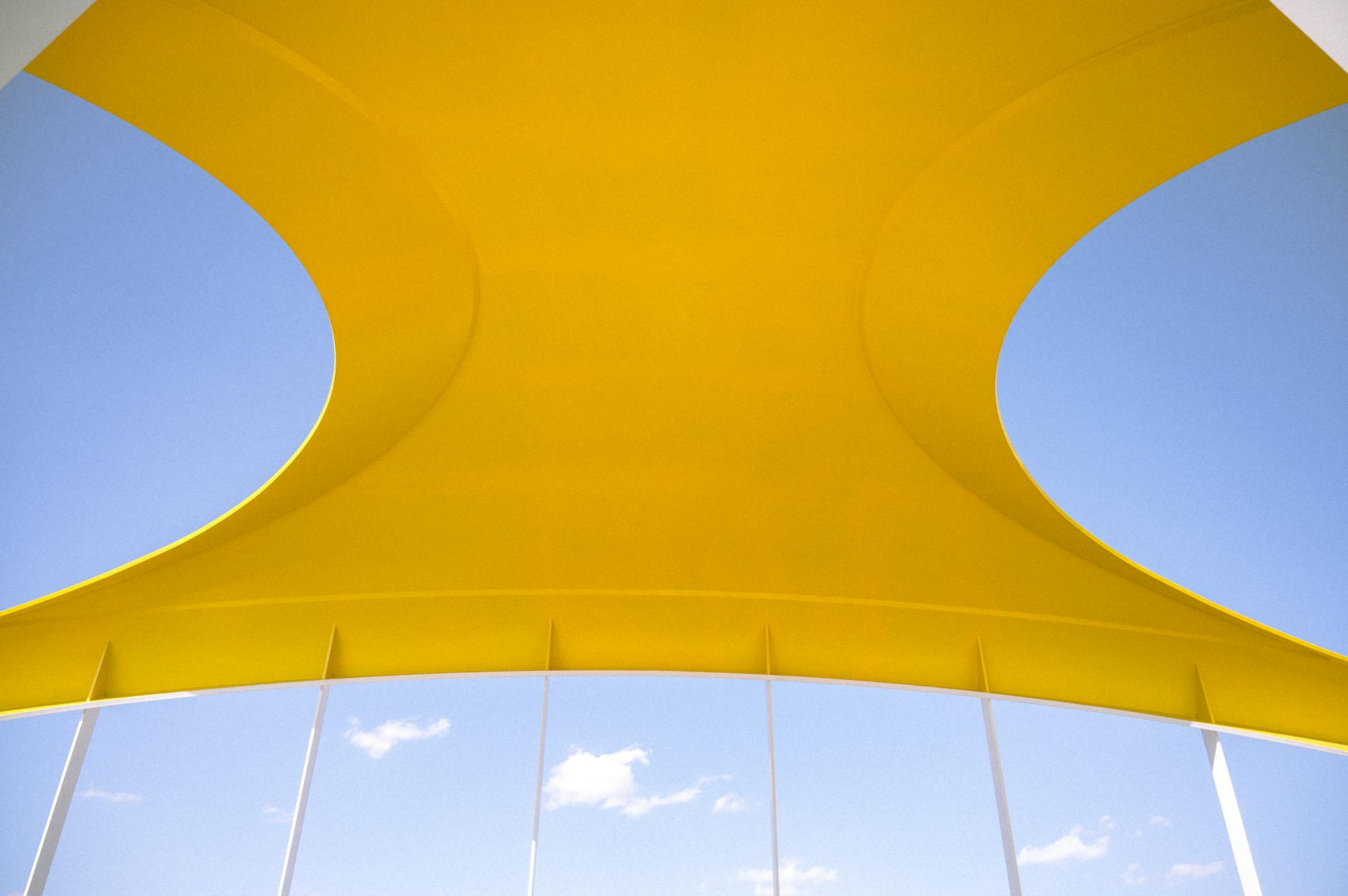 Yellow canopy with modern design over a bright blue sky creating an artistic abstract view.