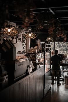 A stylish bakery interior in Anjuna, India with desserts displayed and a customer standing.