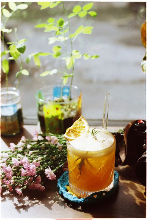 Free A bright citrus cocktail garnished with herbs, surrounded by plants and flowers on a sunny day. Stock Photo