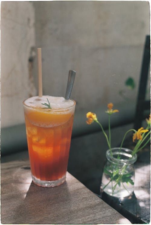 A Glass with Cold Juice and a Little Jar with Wildflowers on a Table 