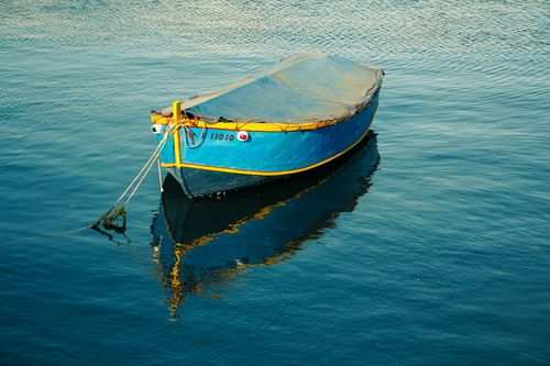 Free A vibrant blue and yellow boat reflecting on calm waters in Valletta, Malta. Stock Photo