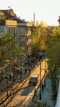 A sunlit urban street with people and a view of a distant minaret at sunset.