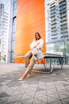 Stylish woman in modern outfit posing outdoors with city buildings backdrop.