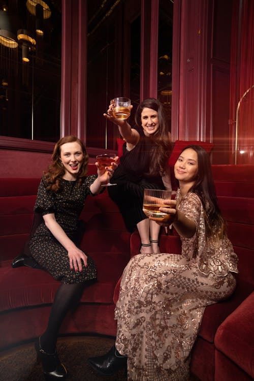 Women Wearing Dresses, Posing with Whiskey in a Dark Red Interior