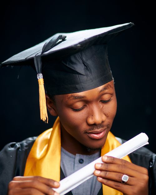 Free Young African graduate in cap and gown holding a diploma, symbolizing educational success. Stock Photo