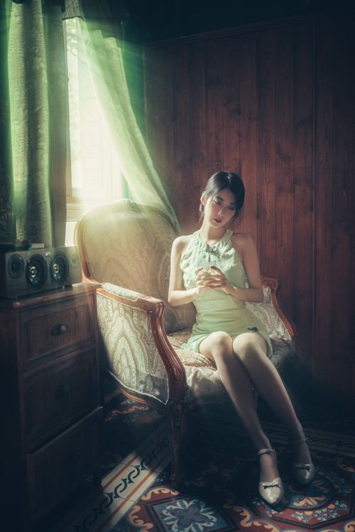 Free A woman in a white dress sits elegantly in an armchair by a window in a vintage-style room. Stock Photo