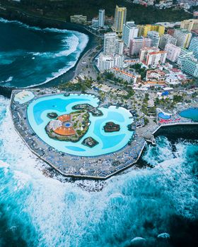 Stunning aerial view of a resort with pools by the coast in Tenerife, showcasing vibrant waves and luxury amenities.