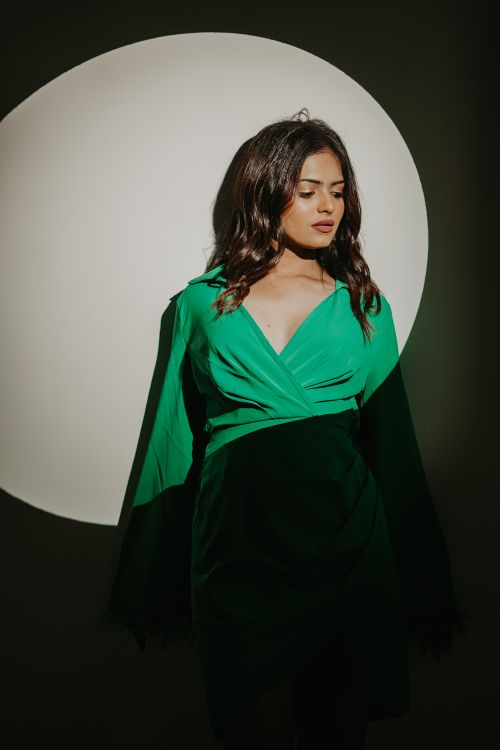 Free A stylish woman poses elegantly in a green dress, highlighted by dramatic spotlight. Stock Photo