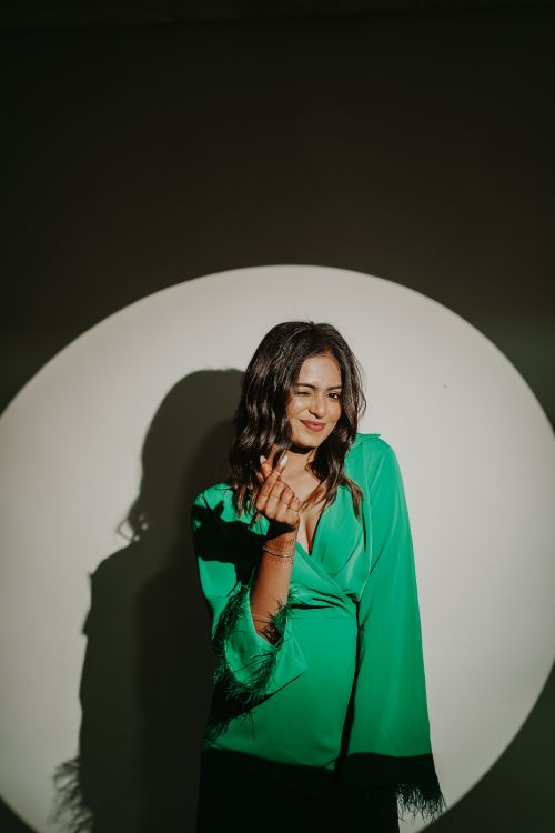 Free Elegant woman in a vibrant green dress posing with a confident smile under a dramatic spotlight. Stock Photo