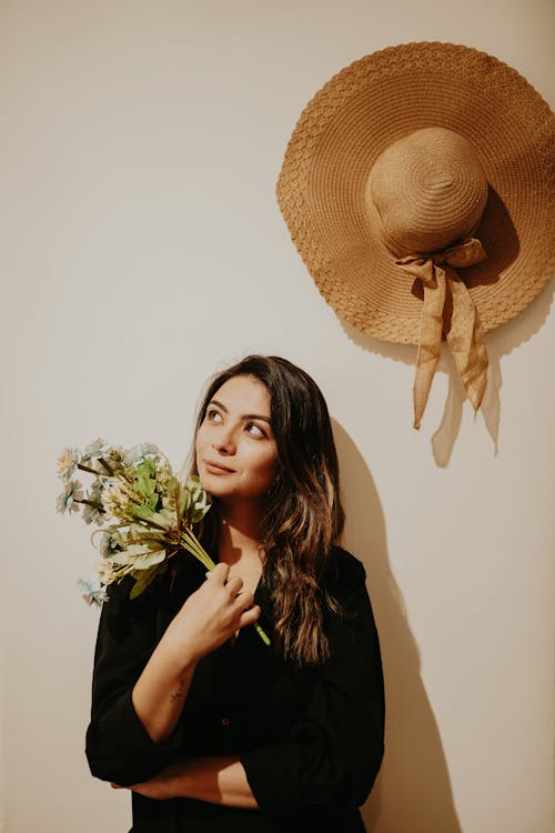 Woman with a Bouquet is Standing Under a Straw Hat Hanging on the Wall