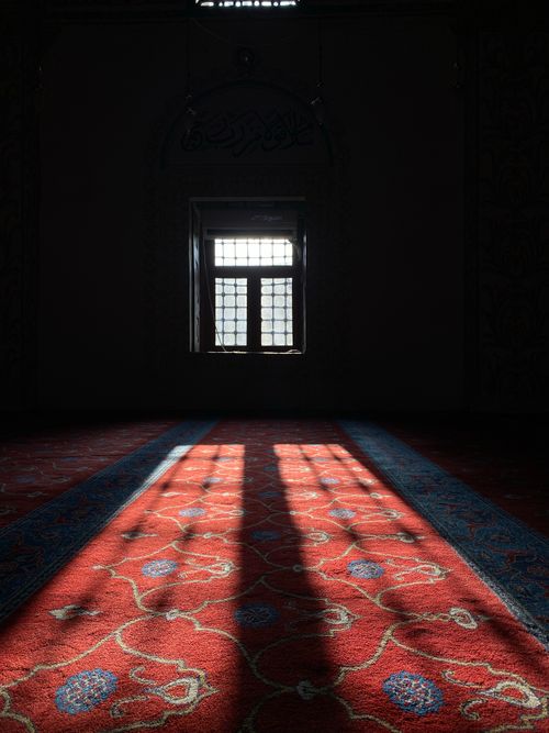 Free Sunlight streams through a mosque window, casting shadows on an ornate carpet. Stock Photo