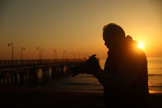 A silhouette of a photographer holding a camera on the beach during a stunning sunset.