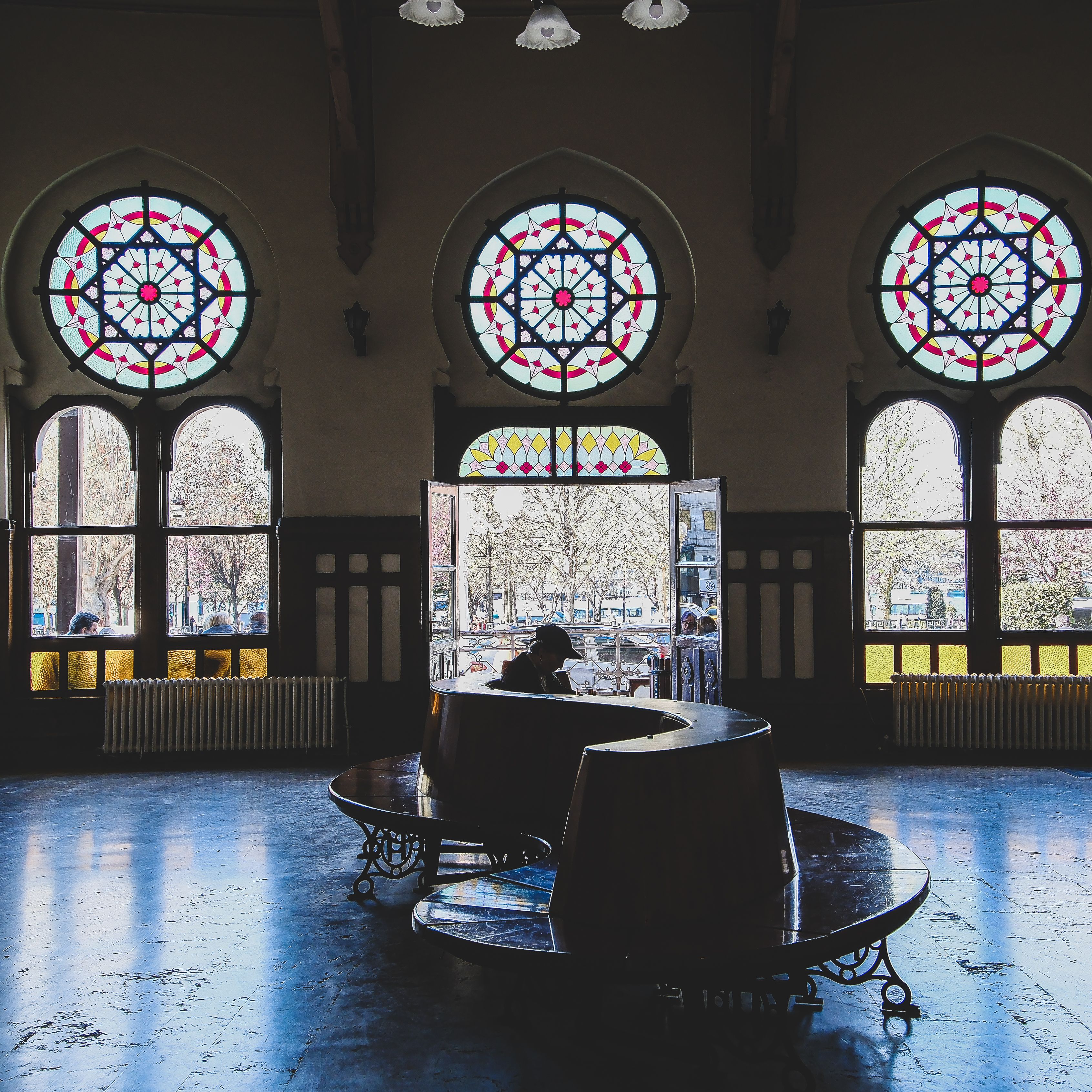 Gothic-style interior featuring ornate stained glass windows with a lone person sitting inside.