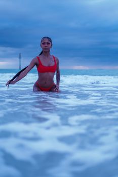 A woman in a red bikini stands waist-deep in ocean waves during sunset, Clearwater Beach.