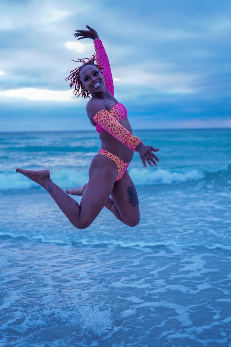 Woman Jumping On Sea Shore Under Clouds