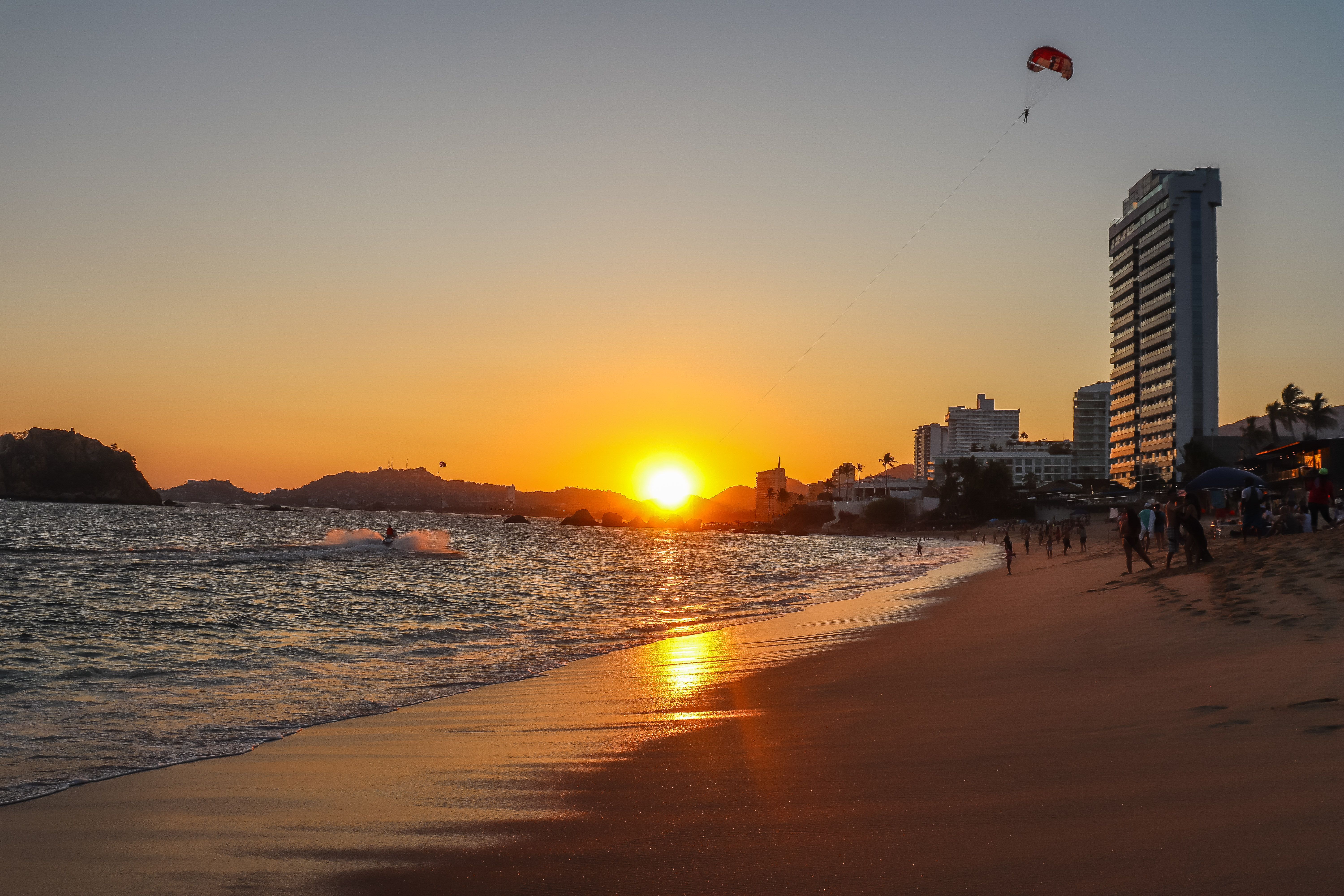 Beach sunset with skyline, paraglider, and scenic view, capturing city's golden hour glow.
