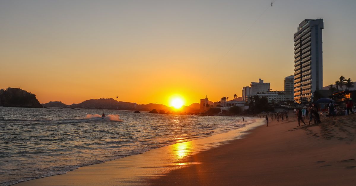 Beach sunset with skyline, paraglider, and scenic view, capturing city's golden hour glow.