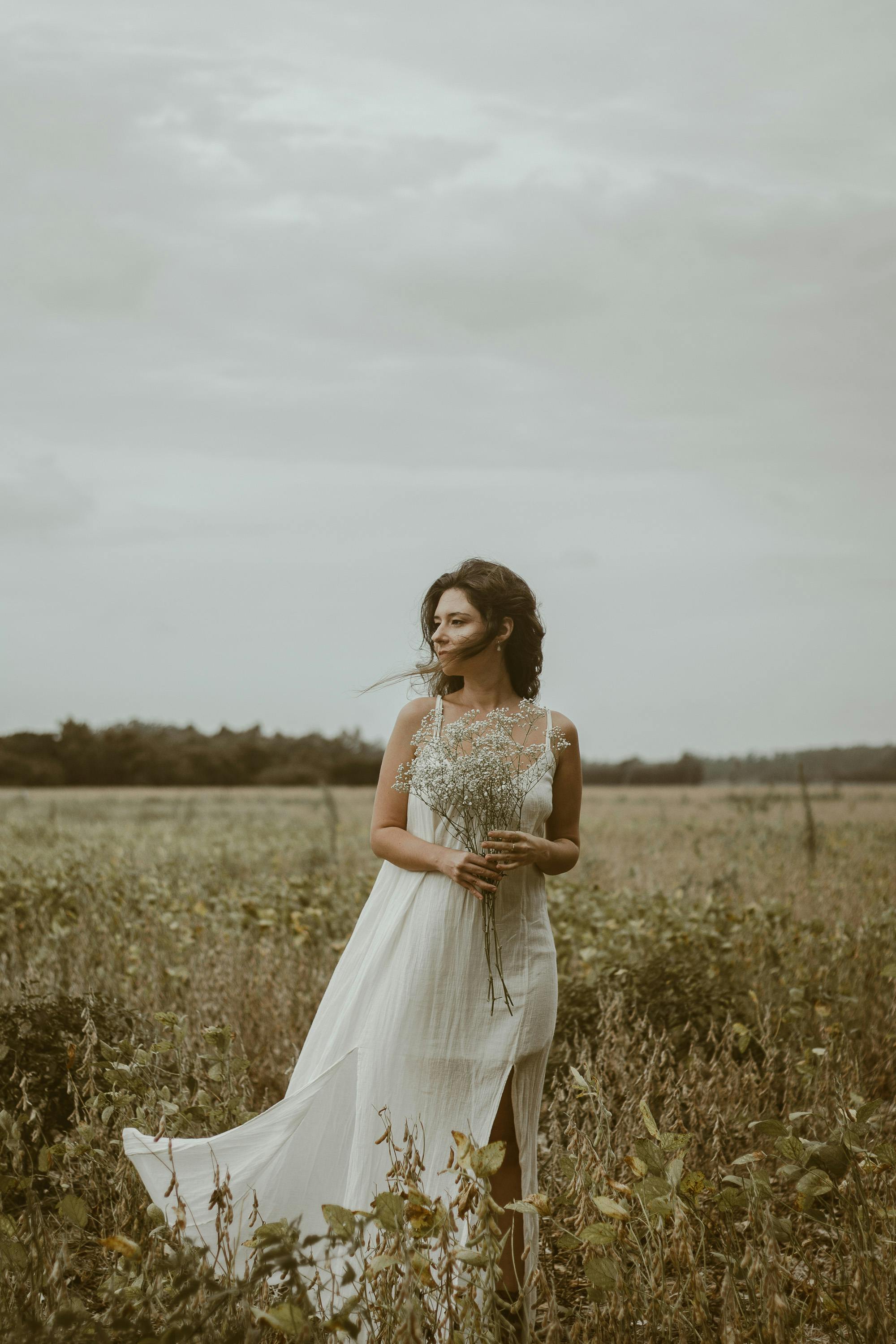 A beautiful portrait of a woman in a white dress standing gracefully in a meadow.