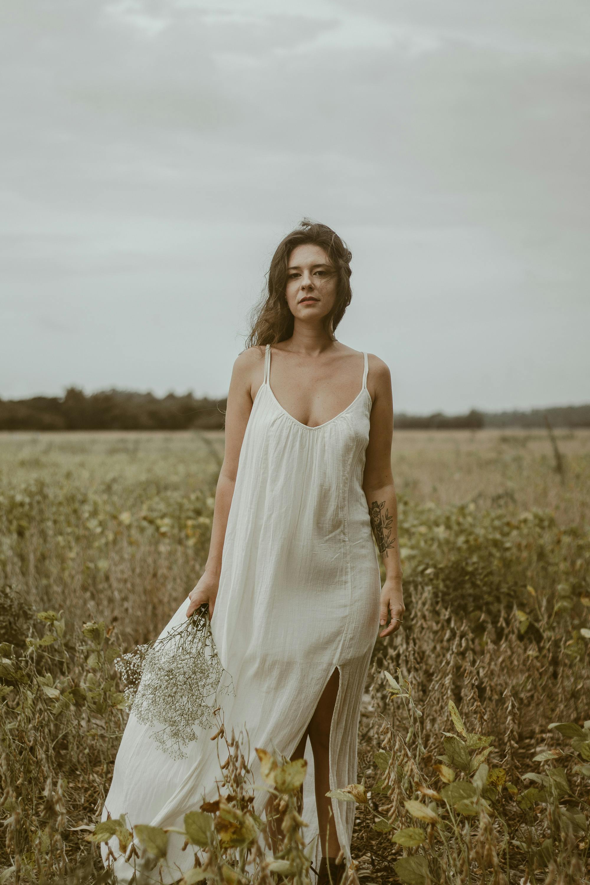 A woman in a flowing white dress stands in a meadow, capturing tranquility and elegance.