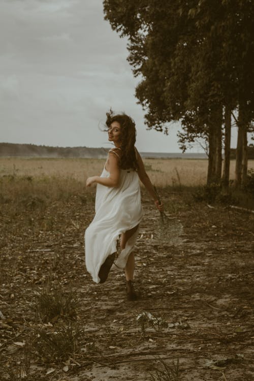 Woman in White Dress Running and Turning Back on Meadow