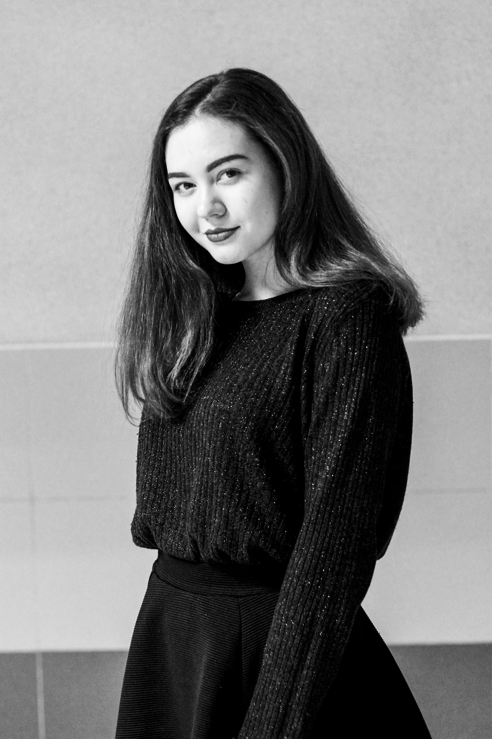 一位穿着时尚针织衫的年轻女子在室内微笑着摆姿势，这是一幅黑白肖像
