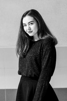 一位穿着时尚针织衫的年轻女子在室内微笑着摆姿势，这是一幅黑白肖像