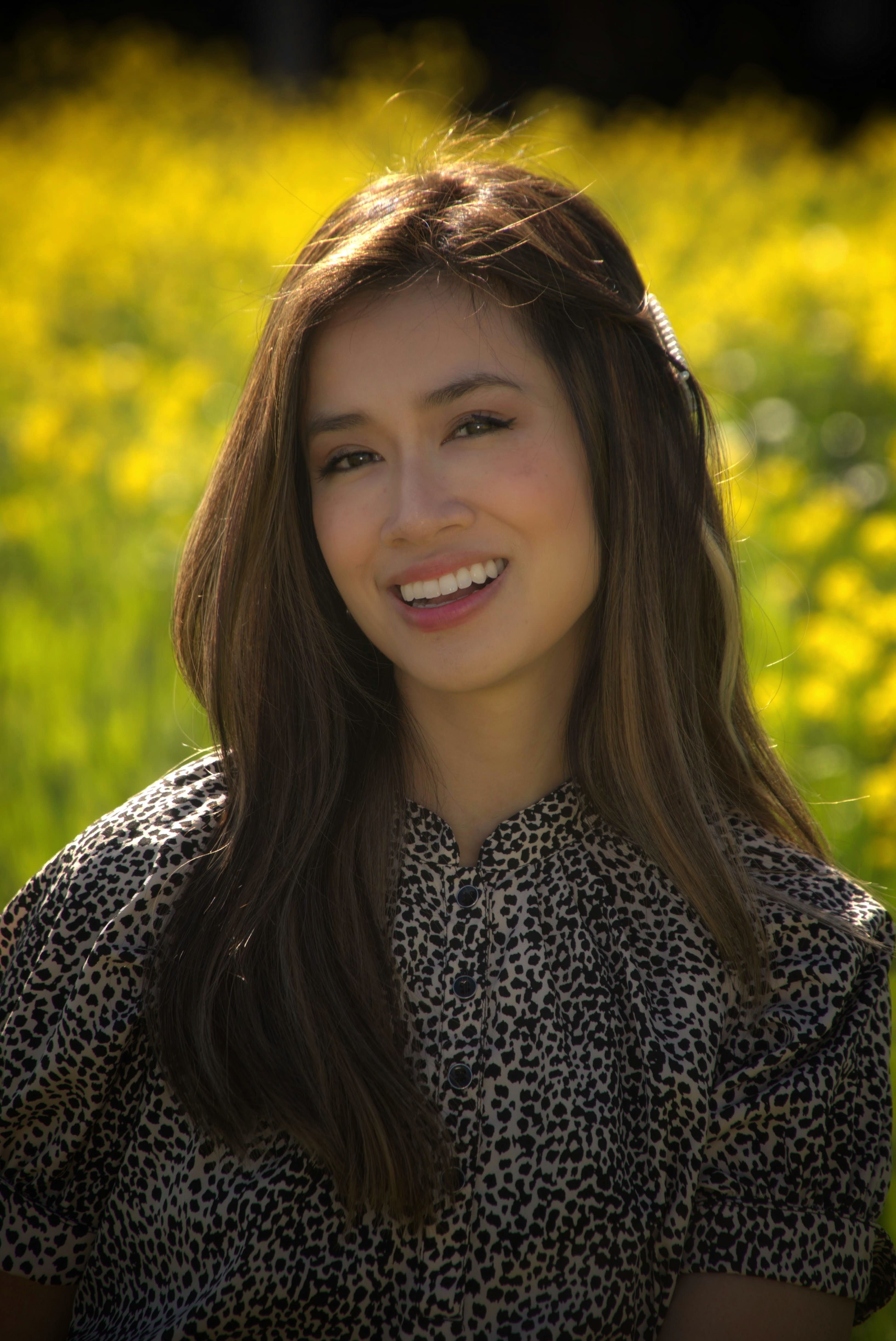 Portrait of a woman smiling in a field of yellow flowers during daytime.