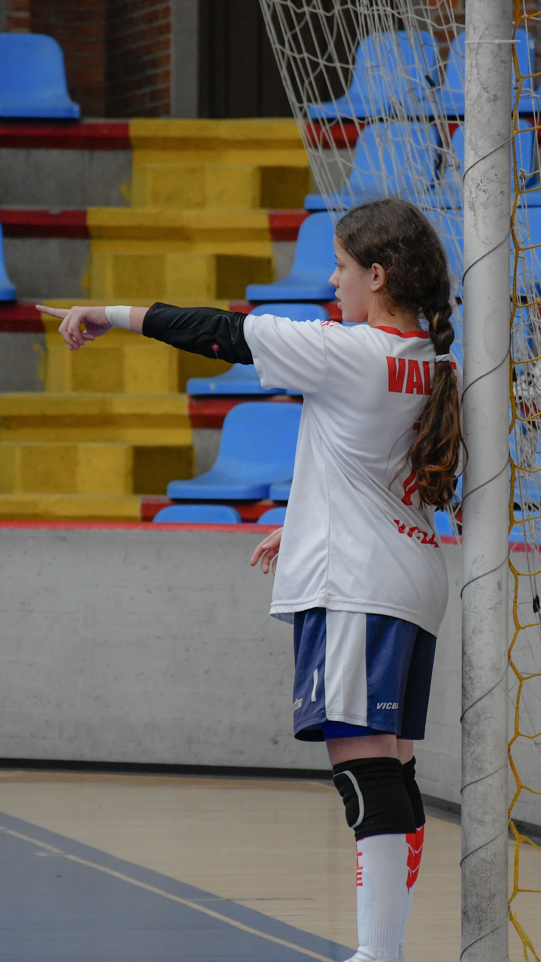 Young girl playing soccer indoors, pointing during a game in a gymnasium.