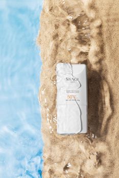 Sunscreen product on sand with flowing water, highlighting SPF 50 protection.