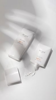 Two SPF 50 sunscreen bottles on a white surface with shadows, minimalist design.