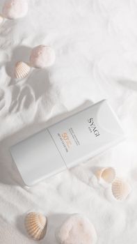 Vertical shot of SPF 50 sunscreen on sand with seashells.