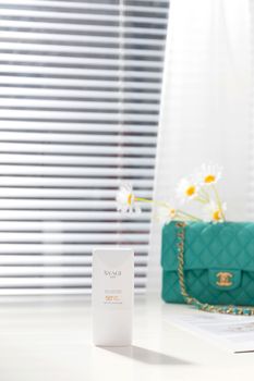 Chic skincare setup featuring SPF 50 sunscreen, a stylish handbag, and daisies.