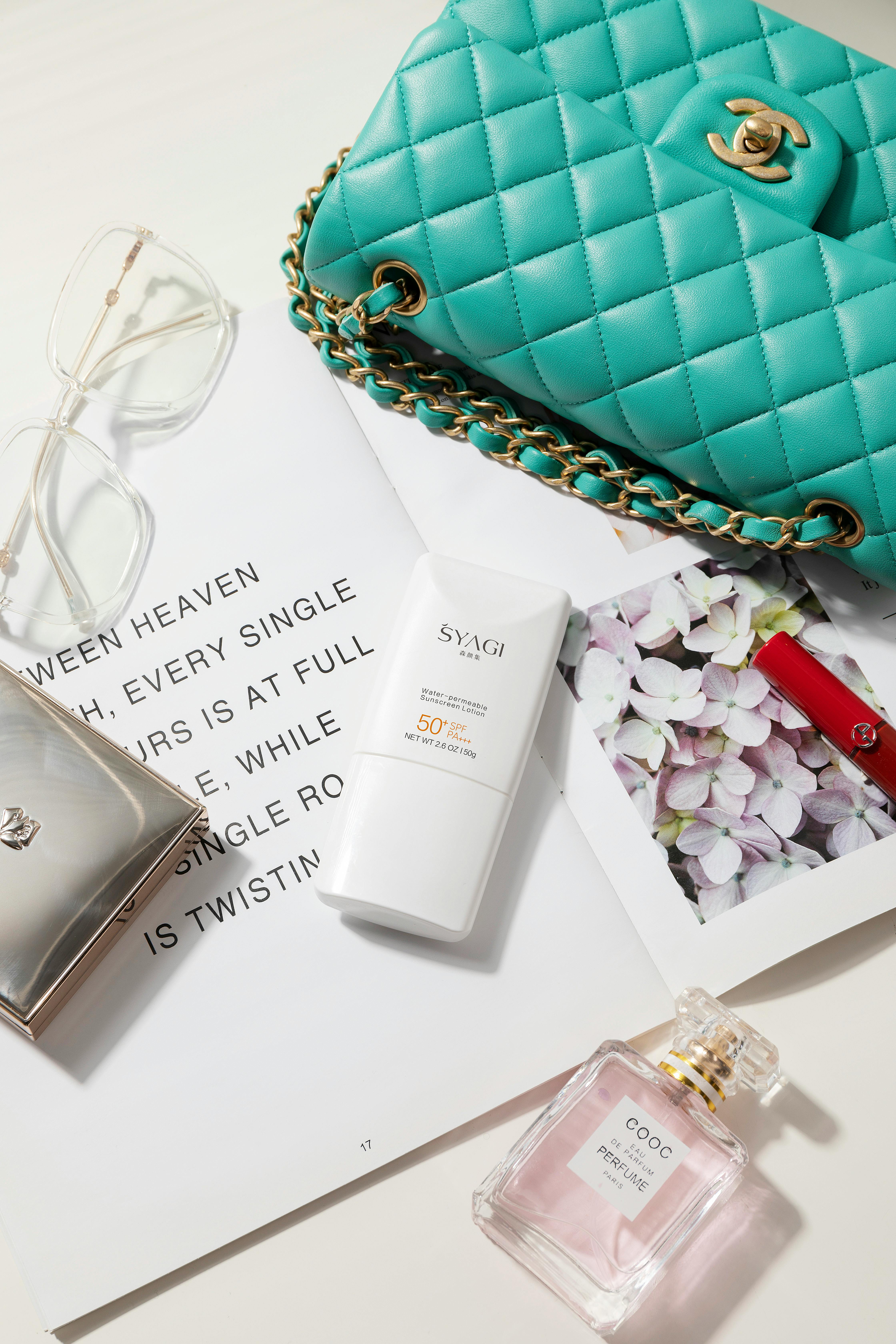 A luxury bag, sunscreen and perfume arranged on a table