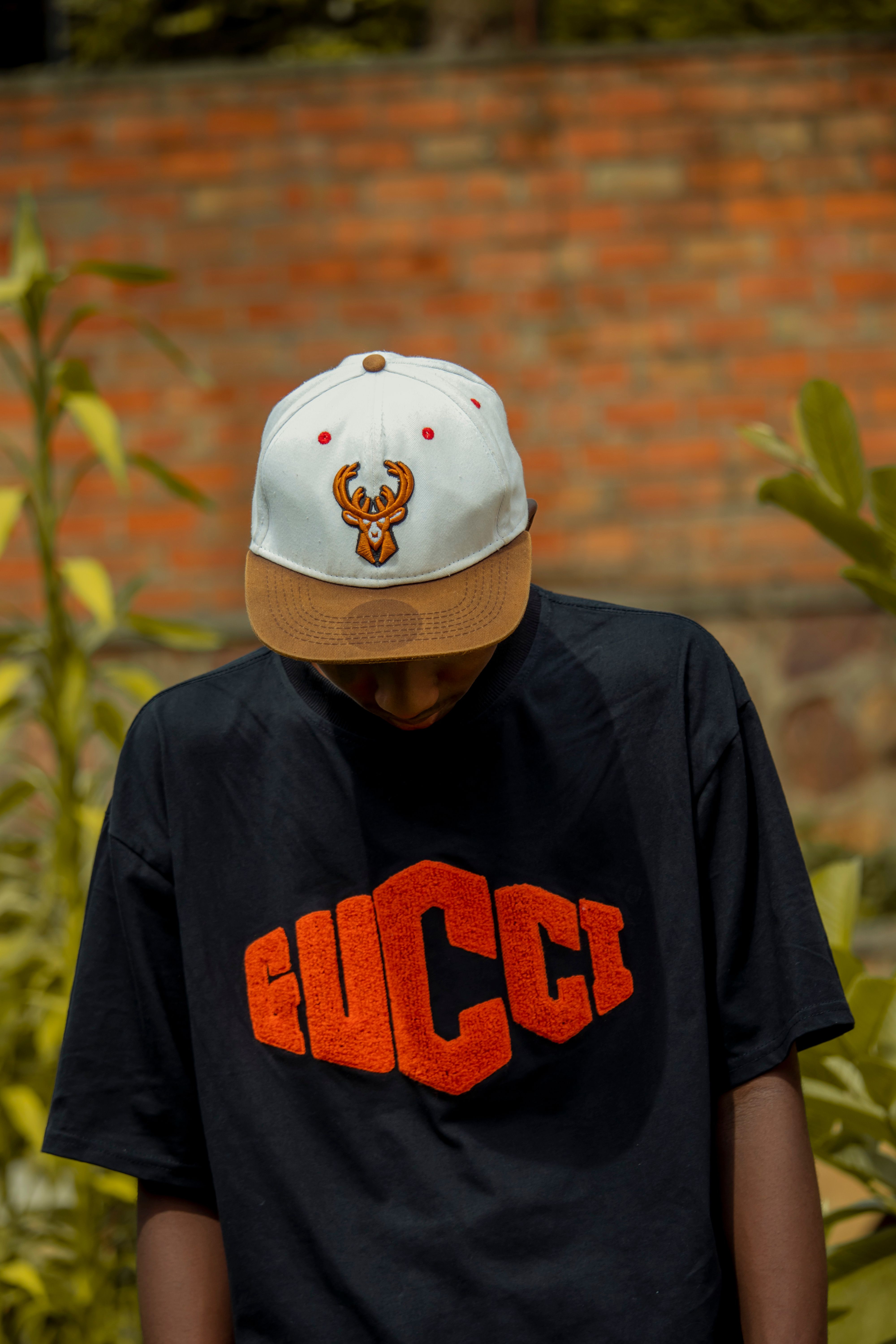 Young man in stylish t-shirt and cap standing outdoors, creating a fashionable look.