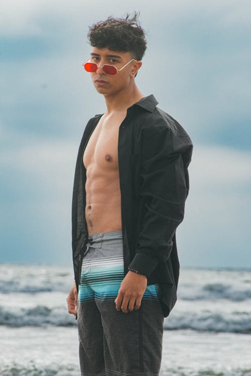 Young Man in Swimming Shorts and Shirt Standing on the Beach 