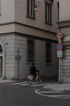 A lone cyclist rides on a city street, surrounded by historic architecture and signage.