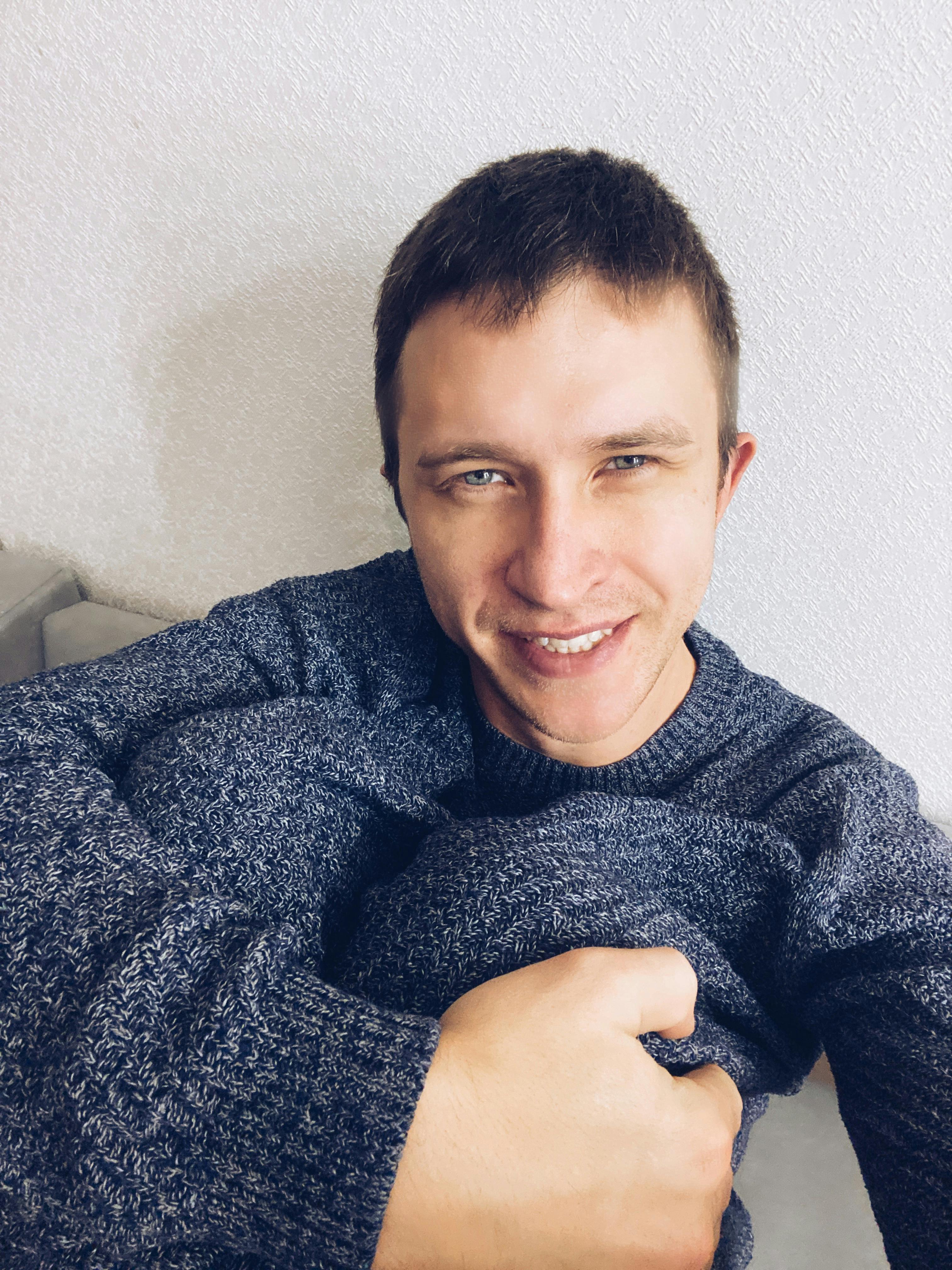 A cheerful man in a gray sweater poses indoors with a warm smile.