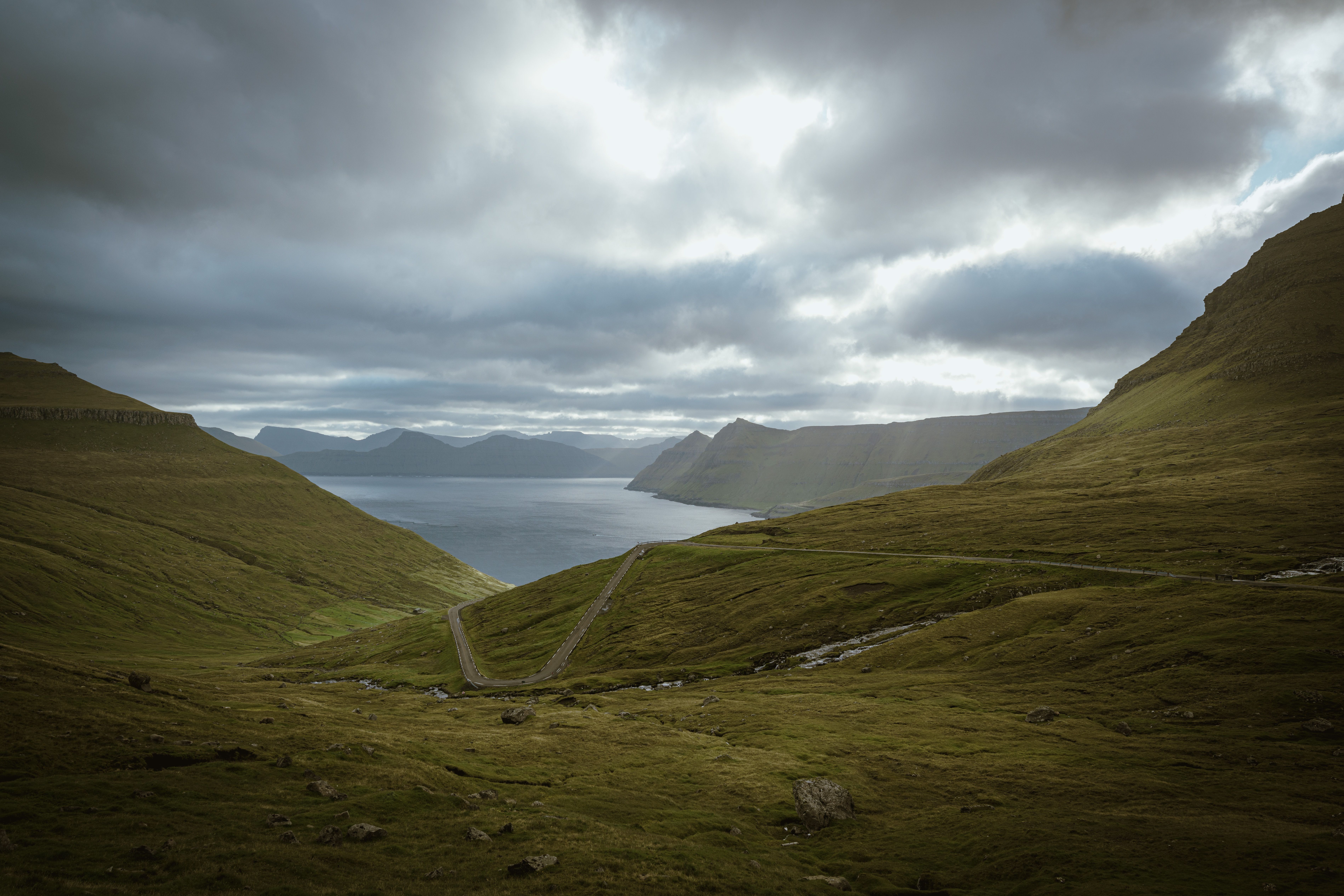A tranquil landscape of green hills, winding road, and ocean under an overcast sky, perfect for nature lovers.