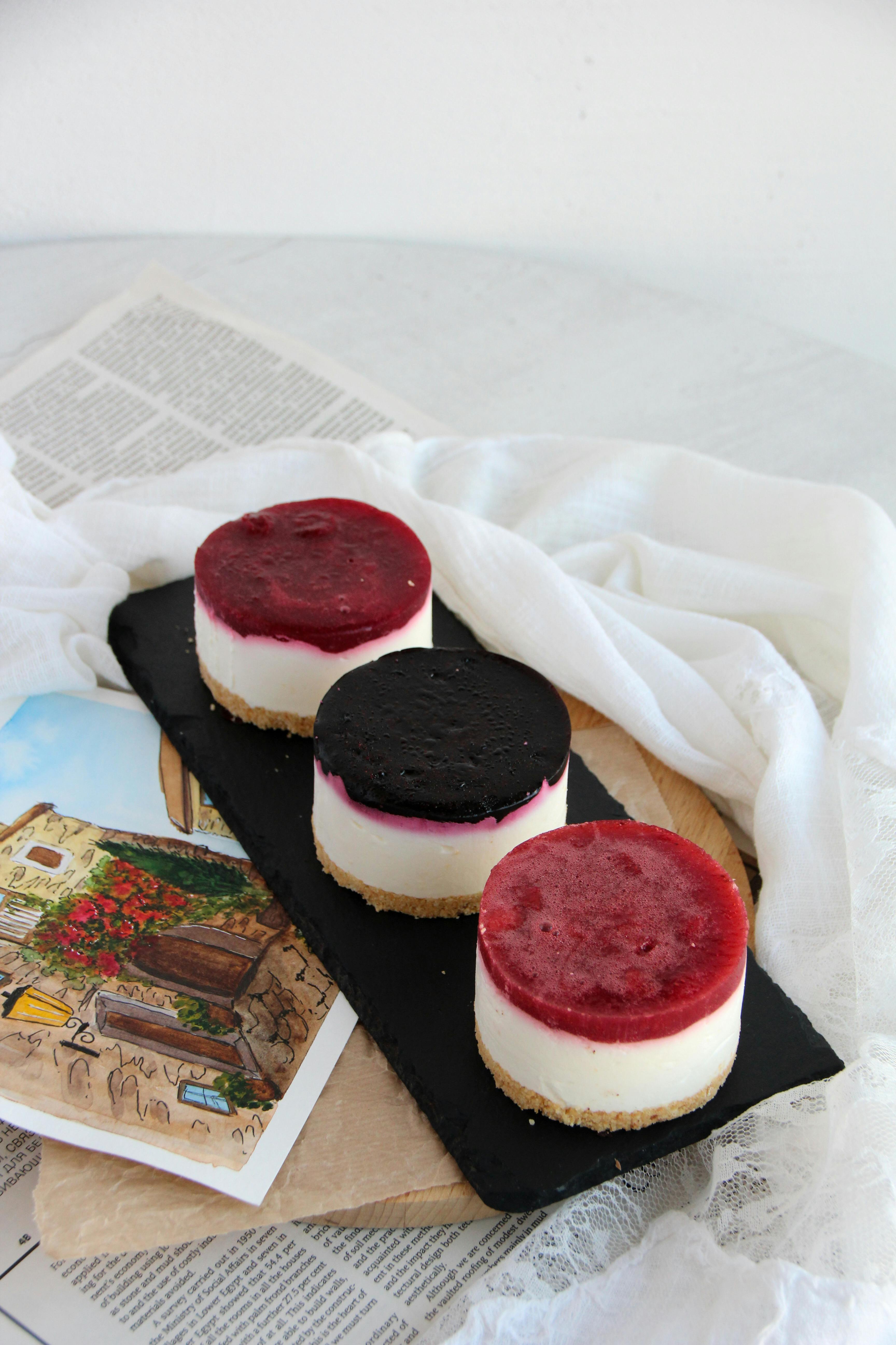 Three mini cheesecakes with fruit toppings on a black slate tray, perfect for dessert presentations.