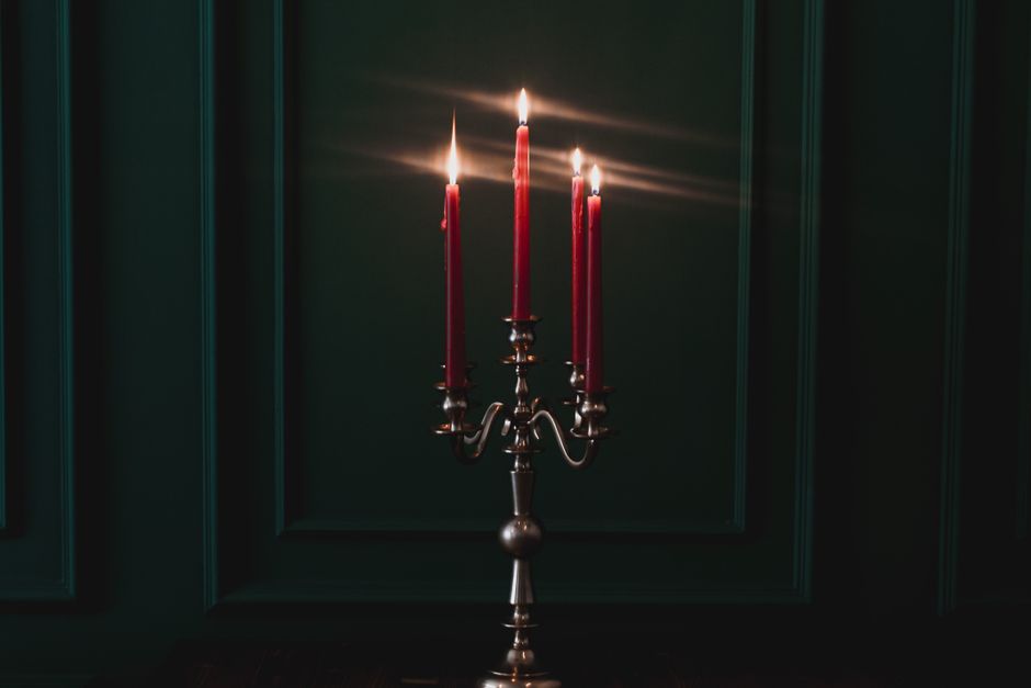 Four lit tapers on a bronze candelabra against a dark panelled wall — photo by Muserref Ikizoglu on Pexels