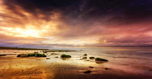 Free A breathtaking sunset illuminating a tranquil beach with boulders and a vibrant sky. Stock Photo