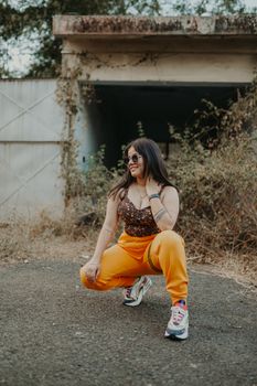 Fashionable young woman in vibrant outfit posing confidently in an urban setting with overgrown plants.