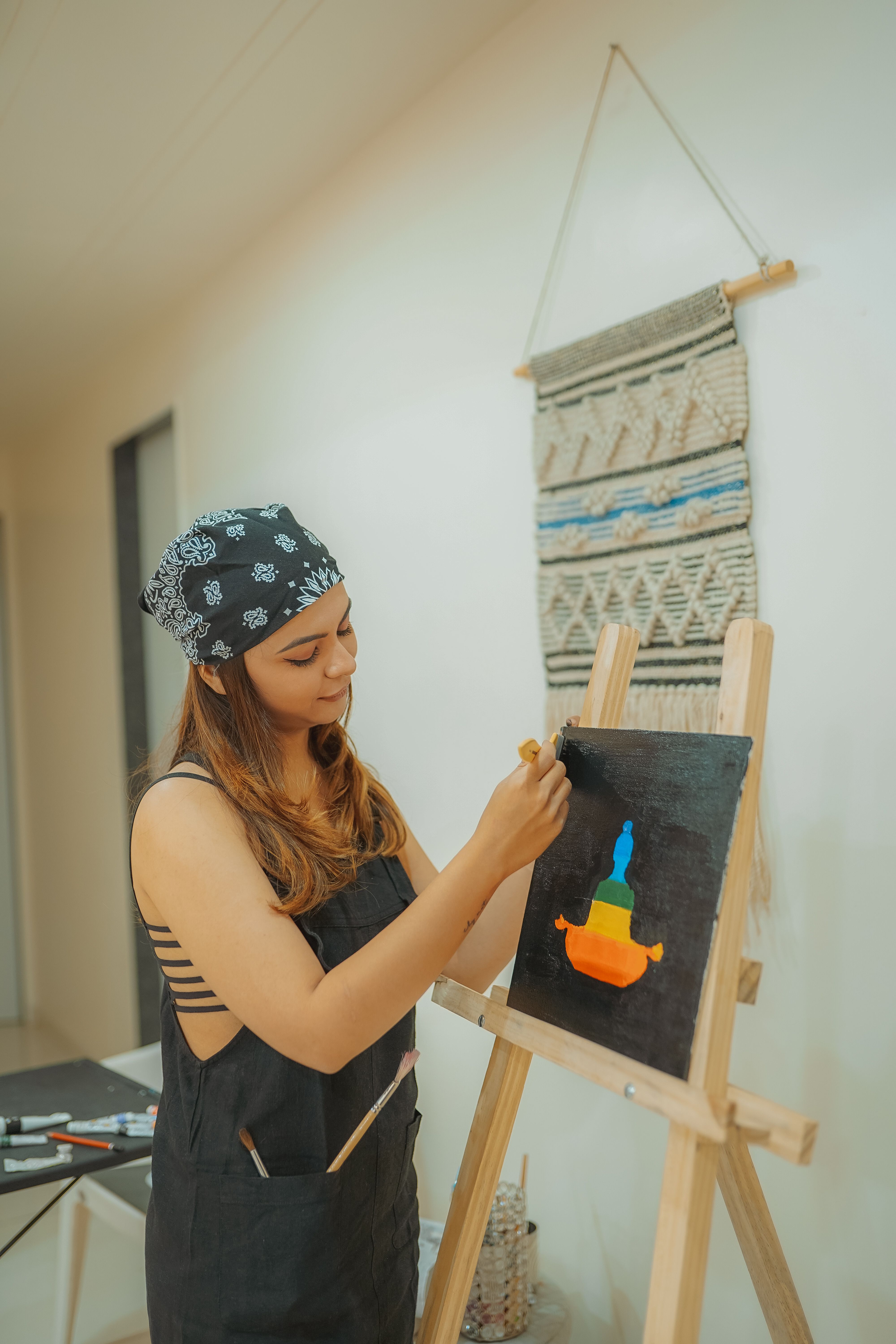 A young woman creatively painting on an easel in a well-lit home studio.