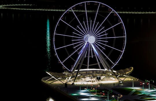 Stunning nighttime aerial view of the illuminated Ferris wheel in Baku, located along the coast.