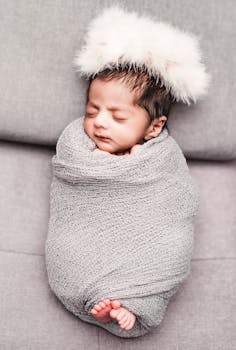 Charming portrait of a sleeping newborn swaddled in a soft gray blanket with a fluffy headband.