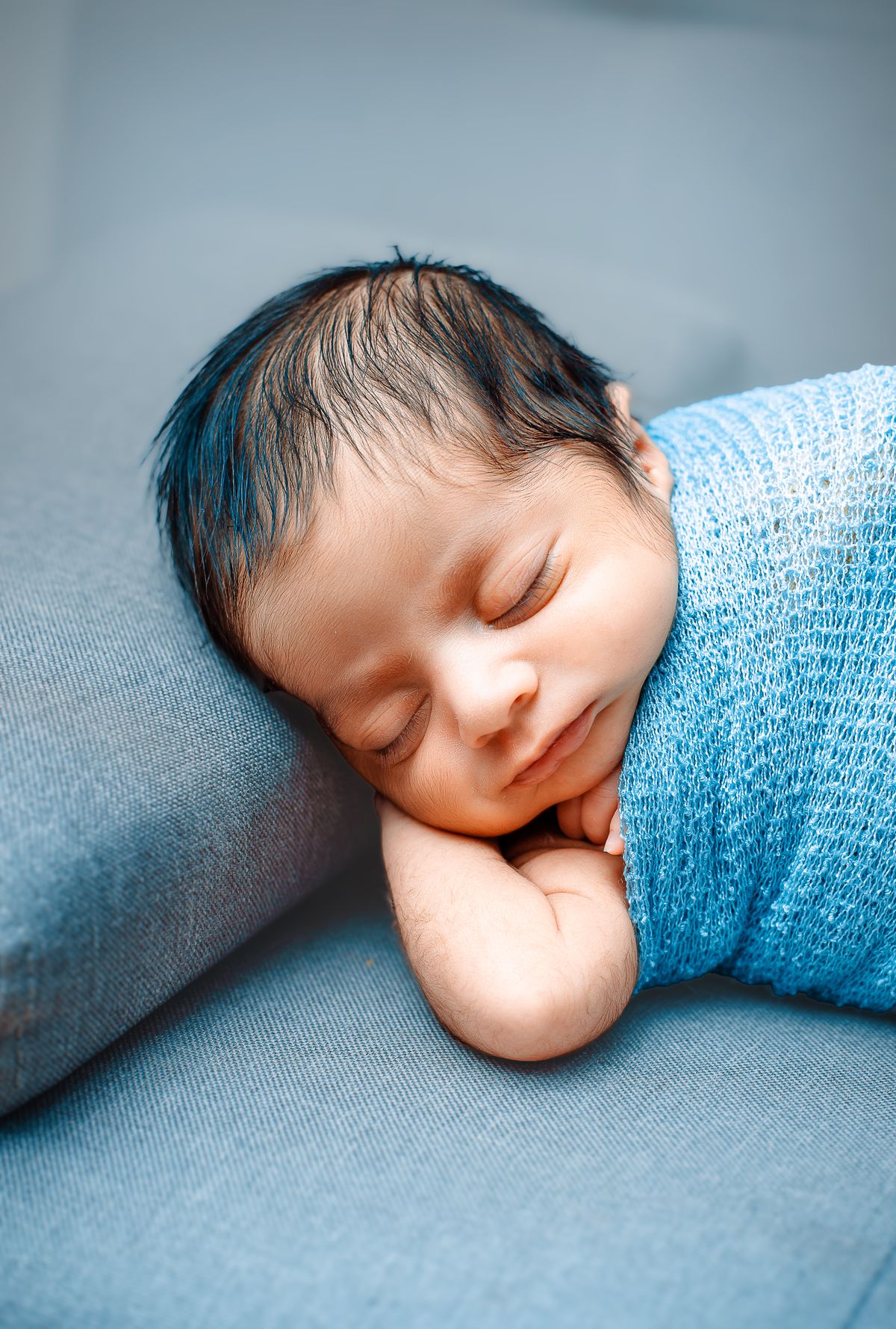 Adorable newborn baby peacefully sleeping wrapped in a soft blue blanket