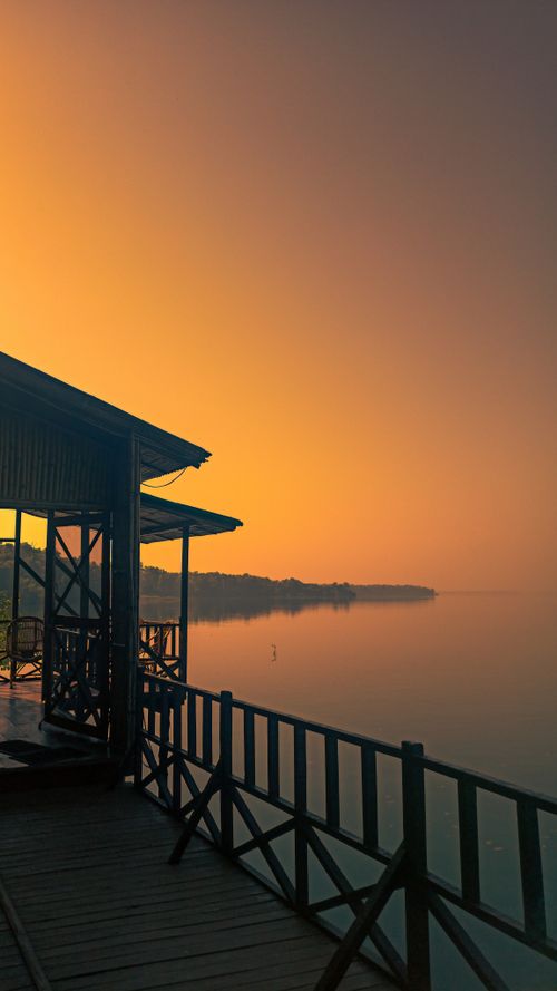 Free Tranquil lakeside view at sunset with a wooden pier in Kanjia Singhpur, India. Perfect for backgrounds. Stock Photo