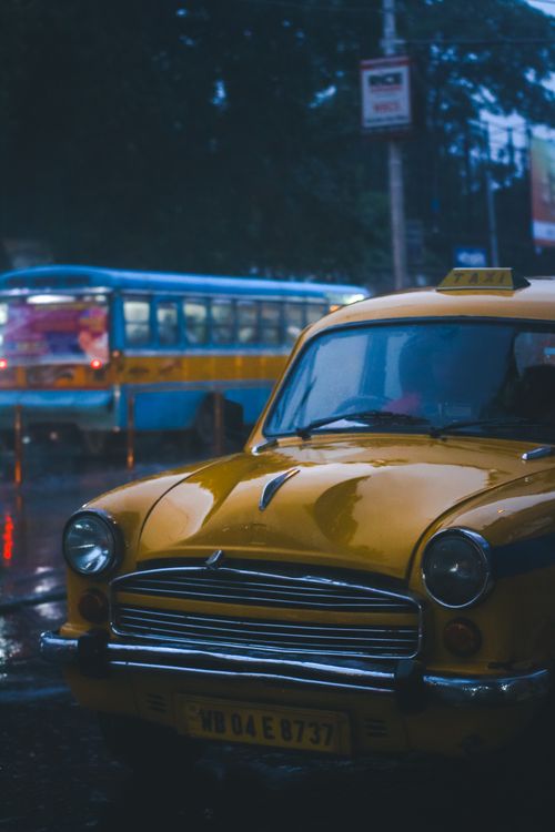 Free Iconic yellow taxi on rain-soaked streets of Kolkata, India, capturing a nostalgic urban scene. Stock Photo